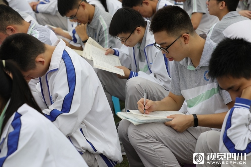 在开学典礼现场,一群拿着课本,练习册埋头学习的学生坐在人群中格外引